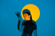 © VISTA by Westend61 - Young woman moving in blue light in front of yellow circle