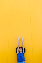 Smiling Woman Reaching Up At Yellow Wall
