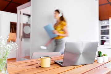 Laptop and mug on desk with blurred motion of woman in background