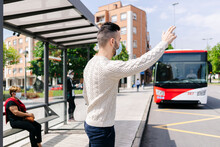 Man Wearing Protective Mask Standing At Bus Stop Hailing Taxi, Spain