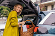 © Westend61 - Portrait of happy woman with protective mask putting purchase in trunk of her car