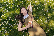 Woman With Let Down Face Mask Enjoying Her Free Time While Lying On Grass With Daisies