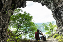 Male Hiker Drinking While Sitting With Backpack At Cave Entrance