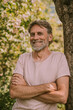 © Westend61 - Happy bearded mature man standing with arms crossed leaning on tree trunk at garden
