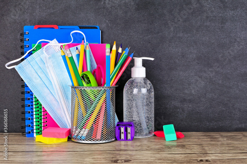 Cuadros en Lienzo School supplies and COVID 19 prevention items on a desk against a chalkboard background