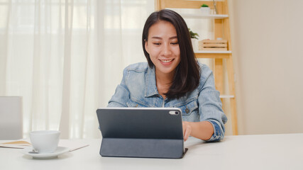 Portrait of freelance smart business women casual wear using tablet working in workplace in living room at home. Happy young Asian girl relax sitting on desk search and do job in internet.