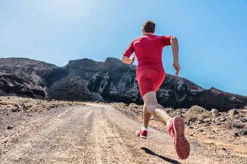 Trail run runner athlete sprinting on rocks path outdoors in mountains landscape. Fit man training in volcanic field for marathon race. Male in compression shorts sportswear clothes running shoes.