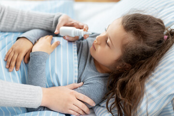 Sticker - family, health and medicine concept - mother with nasal spray treats little sick daughter lying in bed at home