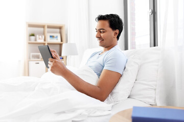 Sticker - technology, bedtime and rest concept - happy smiling indian man with tablet pc computer lying in bed at home