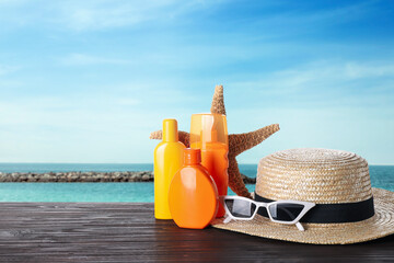 Poster - Set of sun protection products and stylish accessories on wooden table near sea