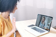 © Vadim Pastuh - Video meeting of employees or friends. A mixed-race woman is greeting young woman on a laptop screen screen. Side view