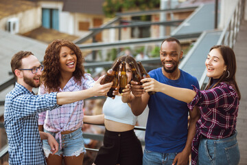 Group of happy friends having beer party in summer day. Resting together outdoor, celebrating and relaxing, laughting. Summer lifestyle, friendship concept. Clinking beer's bottles, look cheerful