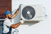 Repairman In Uniform Installing The Outside Unit Of Air Conditioner