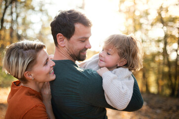 Beautiful young family with small daughter on a walk in autumn forest.