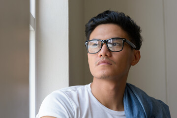 Wall Mural - Face of handsome Asian man with eyeglasses looking outside the window