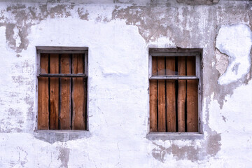 Two windows boarded up by wooden planks in a brick wall of an old building close up