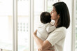 © Yingyaipumi - Close up of asian beautiful mom hugging sleeping newborn baby in her arm and kissing the kid.Asian mother look out the window and holding her baby head in home.she is happy to stay at home with baby.