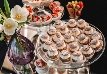 Wall Mural - Wedding dessert, macaroons, meringues, cupcakes, muffins, cakes and sweetness on holiday background with flowers. Candy bar