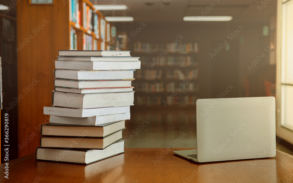 Stack of old books and laptop computer on desk in library background ...