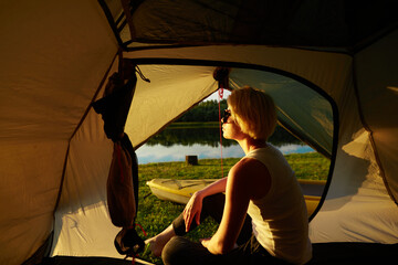 Young woman traveler sitting in the tent, relaxing and with beautiful sunrise