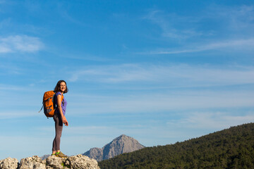 A woman with a backpack stands on top of a mountain and admires the beauty of a mountain valley.