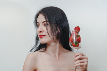 Young woman holding glass goblet of red strawberries in hand. Concept of sexuality, healthy eating