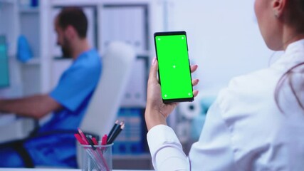 Medical physician holding smartphone with mockup in hospital cabinet while male nurse is working on computer. Healthcare specialist in hospital cabinet using smartphone with mockup.