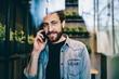 © BullRun - Portrait of handsome bearded young man smiling at camera while calling on modern mobile phone in coworking space.Positive hipster guy dressed in casual wear talking on smartphone device