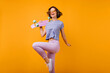 Slim stunning woman in summer attire having fun in studio. Indoor shot of pleased girl with brown hair holding skateboard and dancing.