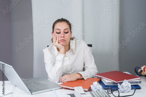 ragazza bionda vestita con camicia bianca è seduta nella sua postazione di lavoro annoiata in mezzo a tutti i documenti e il lavoro da ultimaremare