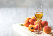 Apricot liqueur in shot glass and fresh apricots on a light wooden table.