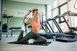 © Drazen - Smiling female athlete stretching while warming up at health club.