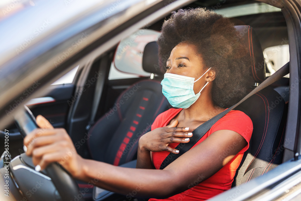 Young attractive african woman with mask on her face driving her car during covid-19 pandemic. - obrazy, fototapety, plakaty 