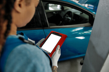 Wall Mural - Young african american woman, professional female mechanic looking at the blank screen of tablet pc, using it at auto repair shop