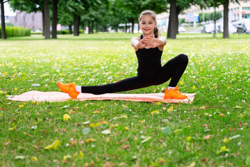 Gymnast schoolgirl warming up in a grass park before performing complex exercises.