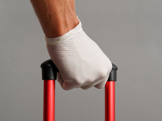 Male hand in glove holds handle suitcase. Travel concept during coronavirus.