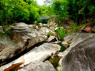 Wall Mural - Hill rocks with waterfall and a bridge up above amid green trees