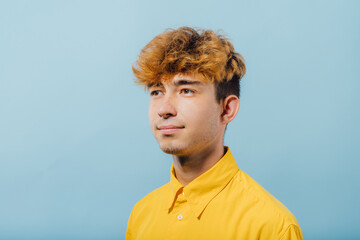 portrait of a nice guy in yellow shirt, young guy, attractive teenager, teenager with fashionable hairstyle, blue background, studio shot