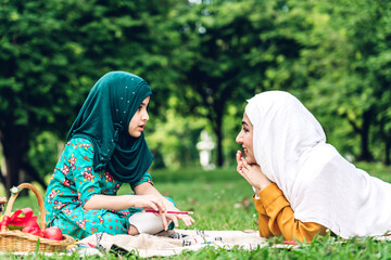 Wall Mural - Portrait of religious enjoy happy love asian family arabic muslim mother and little muslim girls child with hijab dress smiling and having fun moments good time in summer park