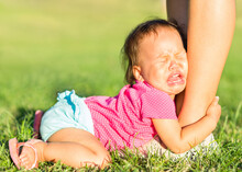 Crying Child Attached Onto Parents Legs Throwing Tantrums At The Park. Family And Childcare.
