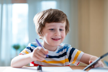 Wall Mural - Back to school. Distance learning online education. Caucasian smile kid boy studying at home with smartphone and doing school homework. Smiling child siting at table with cell phone