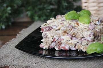 Salad with scallops, cheese and beans, decorated with two Basil leaves on a black plate