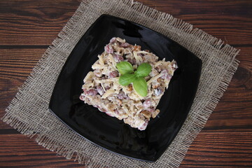 Salad with scallops, cheese and beans, decorated with two Basil leaves on a black plate