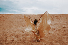 A Beautiful Girl In A Golden With Brilliant Dress With Wings, Suit Is Dancing An Oriental, East Dance In The Desert.
