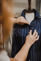 Poster - Vertical shot of a female fixing a blue striped shirt on a mannequin