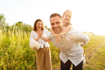 Cheerful dad piggybacking his little daughter in countryside