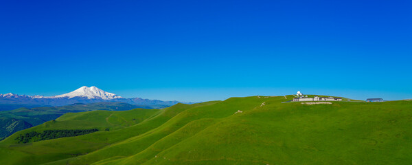 Wall Mural - Green Meadow Hills background Elbrus at a Summer Day. Panorama