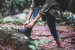 Closeup image of a woman hiker tying shoelaces and getting ready for trekking in the forest