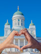 Close-up, fingers make a heart shape. Hand of a white and black man. Blurred background Cathedral, White Church in Helsinki. The main tourist destination.