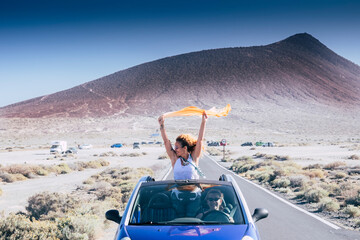 Wall Mural - Happiness and travel lifestyle concept with beautiful woman outside a convertible blue car enjoy the freedom and have fun on the road with her female friends driving the vehicle - friends and life